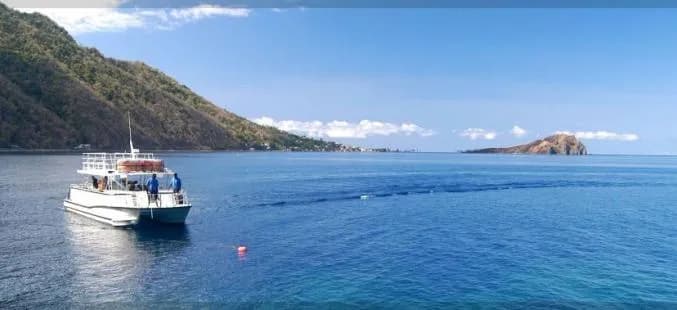 A boat floats on calm water, with a majestic mountain rising in the background under a clear blue sky.