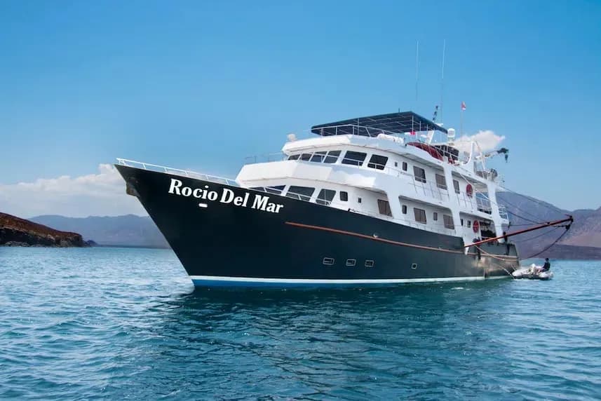 A large boat named Rocio del Mar sails in the ocean, with majestic mountains rising in the background.