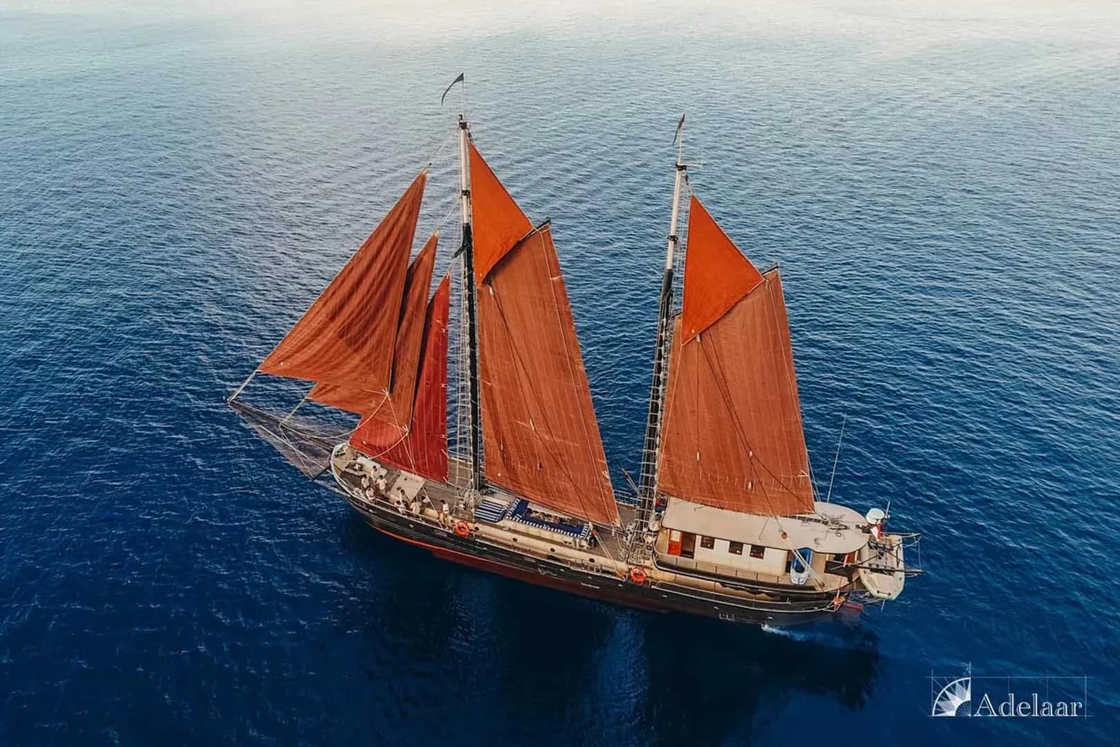 Aerial view of the Adelaar sailboat with red sails gliding across the ocean's surface.