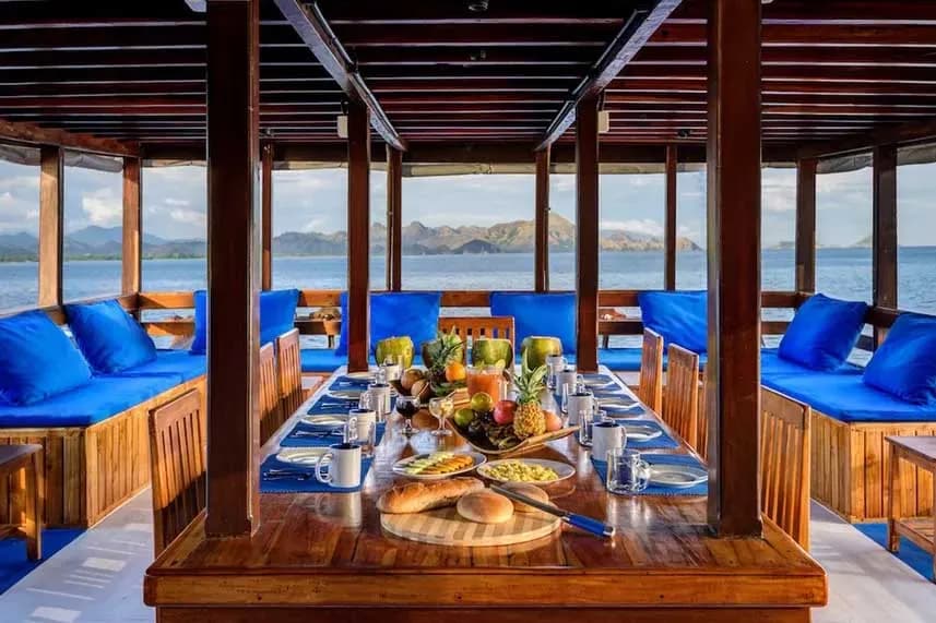 A dining table on a boat, adorned with blue cushions and pillows, set for a meal on the Mari Liveaboard.