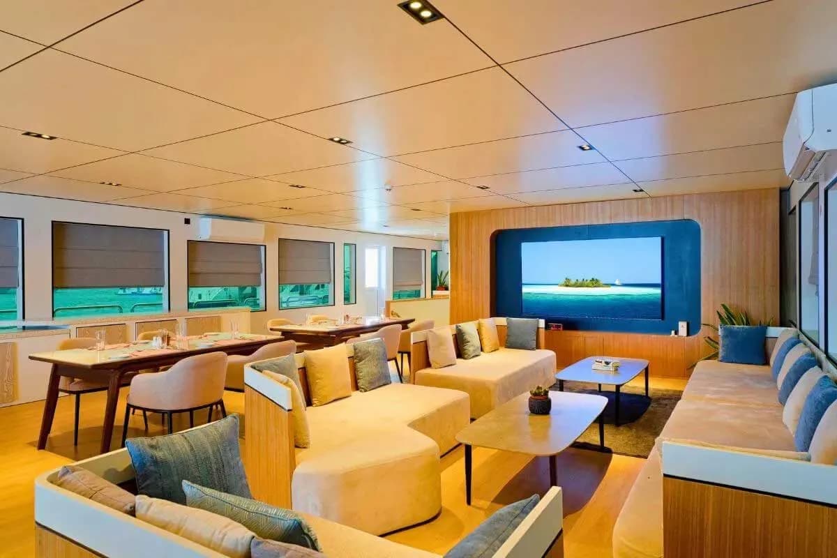 The living room of the Ariyal Liveaboard features comfortable couches and chairs, creating a cozy atmosphere.