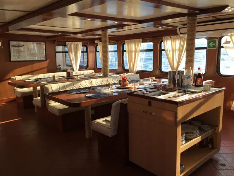 Dining room interior with booth-style dining tables next to large windows aboard the MV Valentina liveaboard.