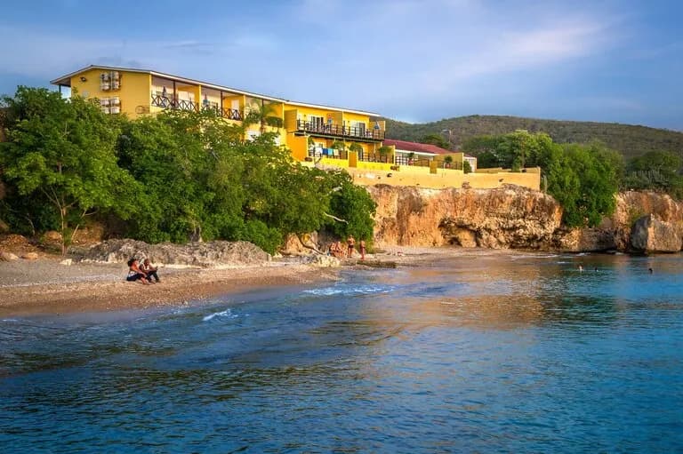 A serene beach and resort at sunset, with golden hues reflecting on the calm waters.